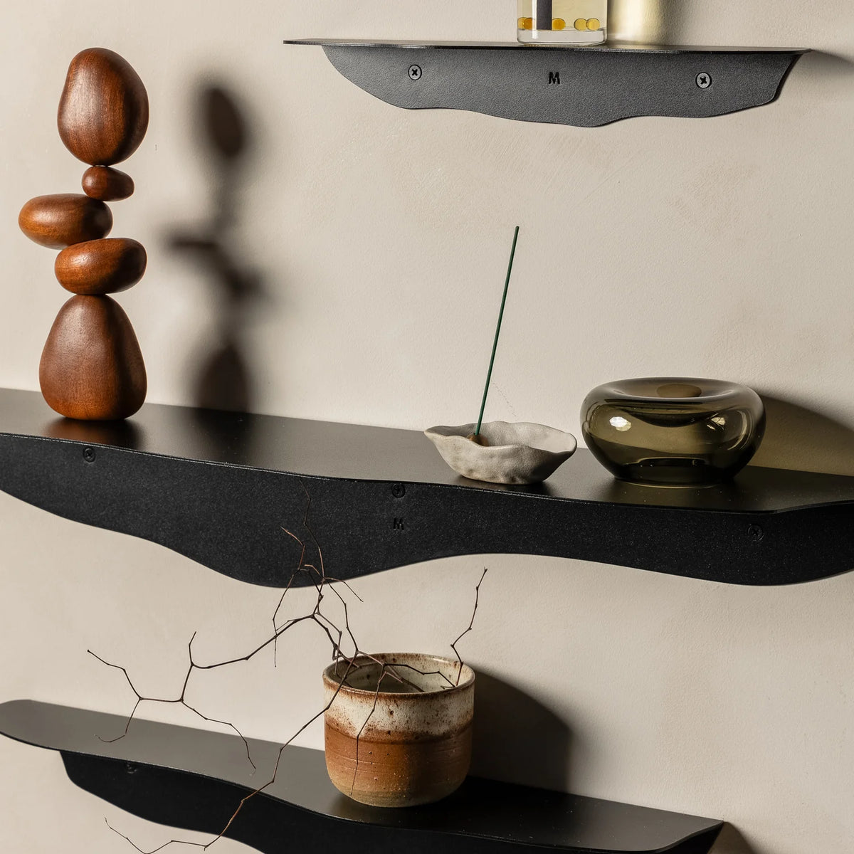 Close view of black wavy shelves with a stacked pebble sculpture, a brass bowl and an amber candle