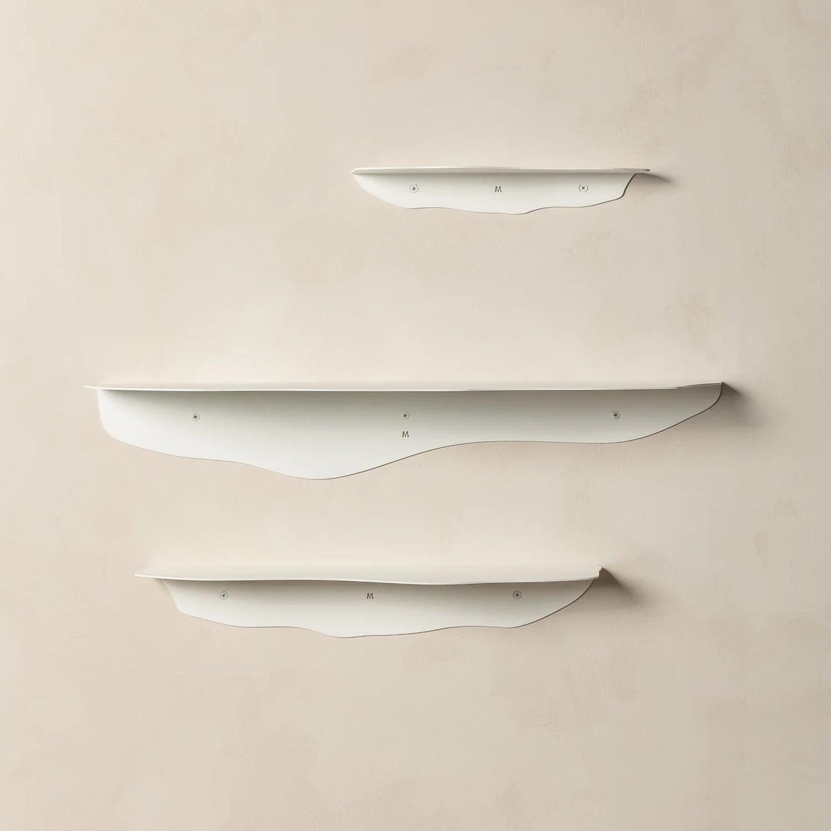 Three empty white wavy shelves staggered on a warm beige plaster wall with soft shadows beneath