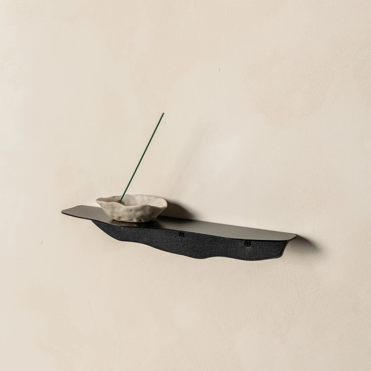 Black wavy shelf from further back at an angle, holding the same stone dish and incense stick