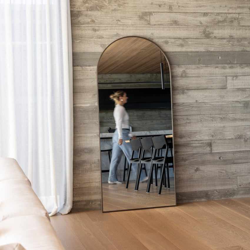 Framed Arch full length mirror leaning against a timber panelled wall, reflecting a woman standing at a kitchen island