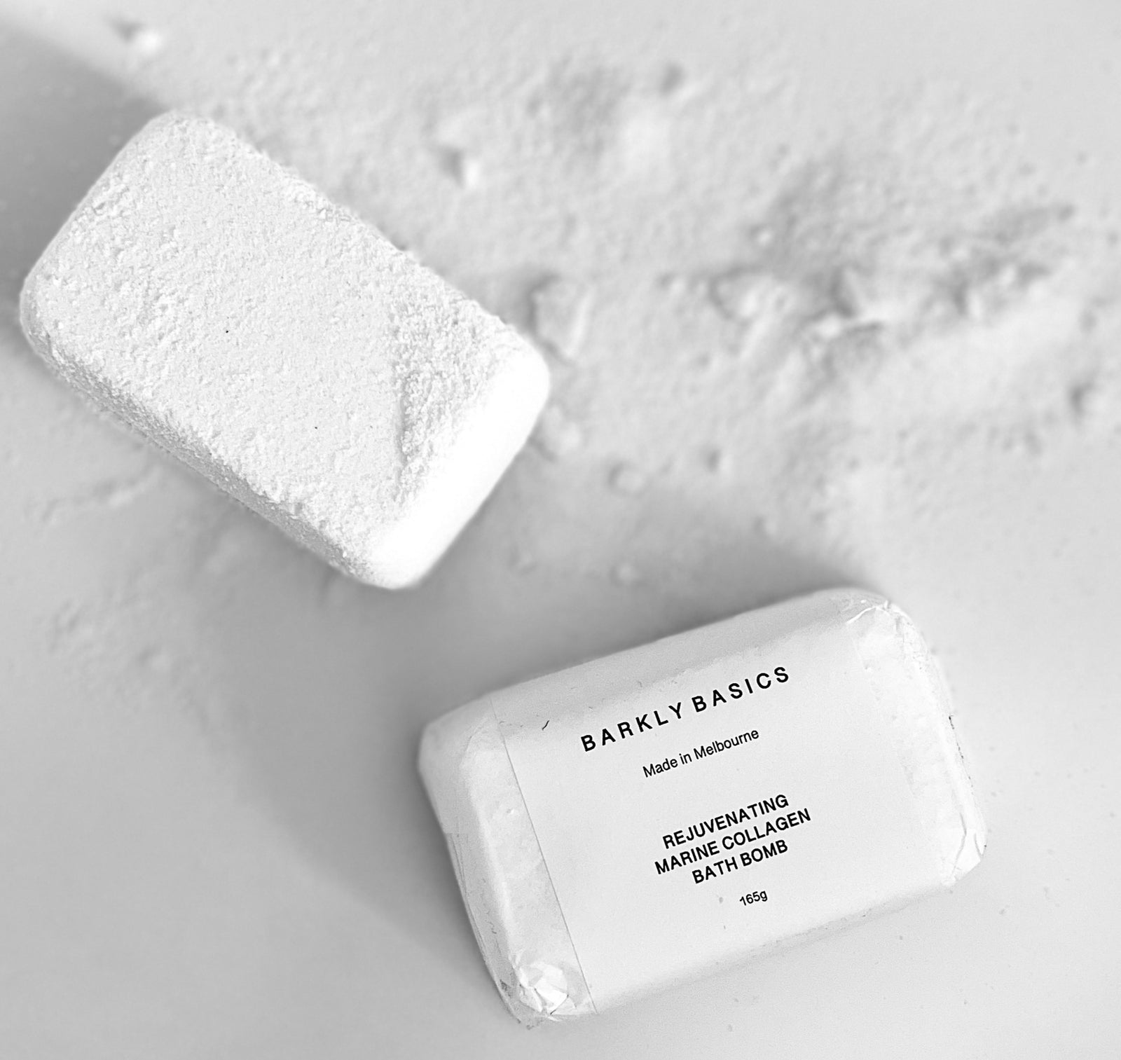 Flatlay of Barkly Basics Rejuvenating Marine Collagen Bath Bombs, with one unwrapped and crumbled on a white surface, highlighting the textured, powdery finish