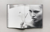 A black and white photo of a woman holding KATE: THE KATE MOSS BOOK.