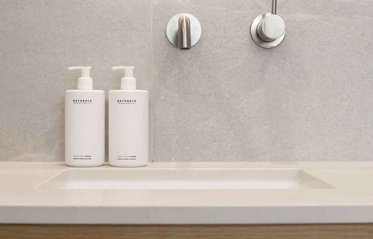 Two Naturals pump bottles on a stone vanity below brushed steel wall tapware