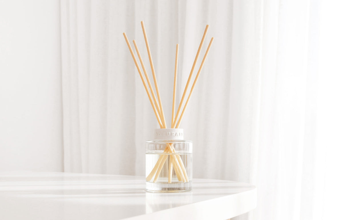 Reed diffuser on a white table in front of sheer white curtains