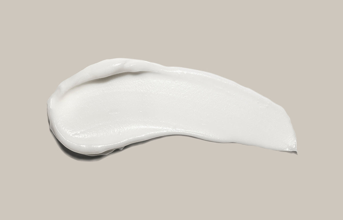 Swatch of white hand cream smeared across a warm grey background