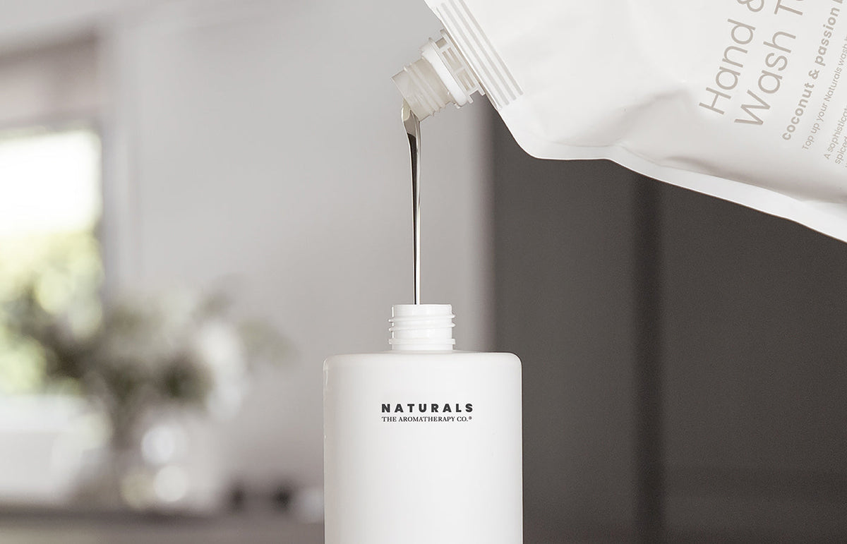 Wash pouring from a refill pouch into an open Naturals bottle, landscape crop