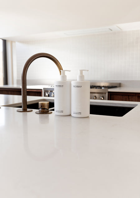 Two Naturals bottles by a bronze tap at an undermount sink on a white bench