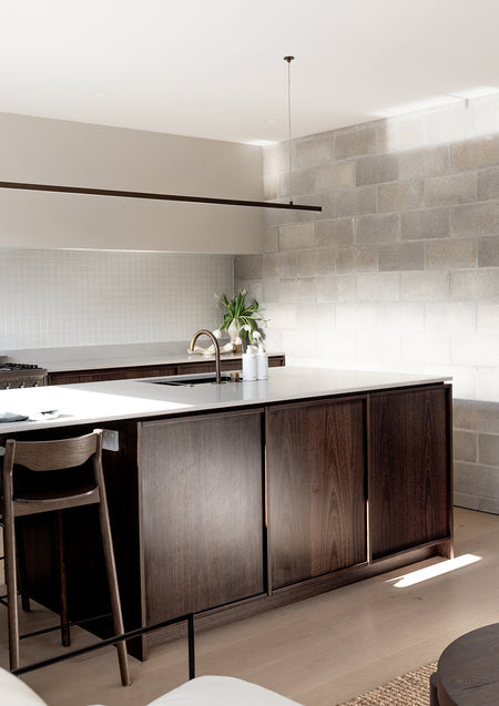 Dark timber kitchen island with a white bench top, two pump bottles and pendant lighting