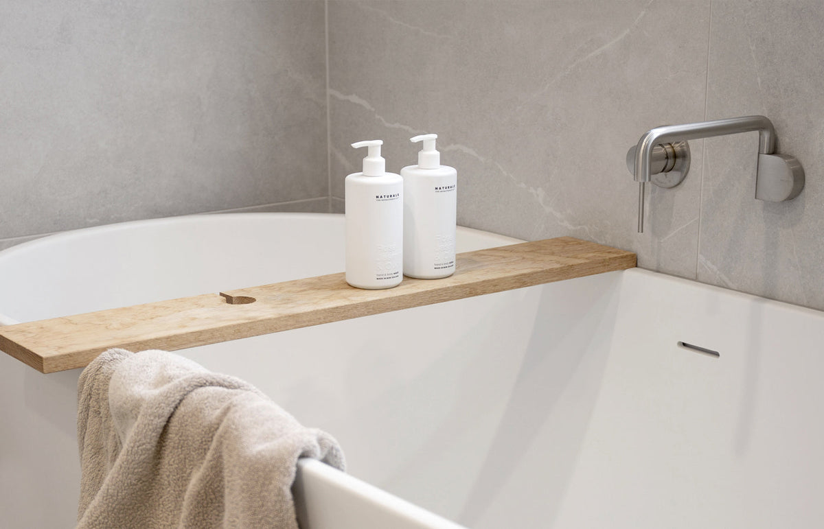 Two white pump bottles on a timber bath caddy across a white bath with a towel draped over