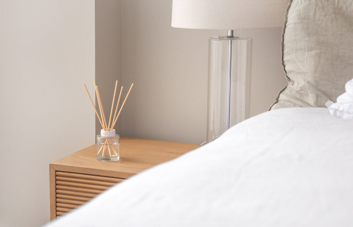 Naturals diffuser on a fluted bedside table beside a glass lamp and white bedding