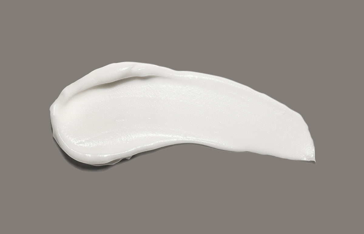 Swatch of white hand cream smeared across a warm grey background