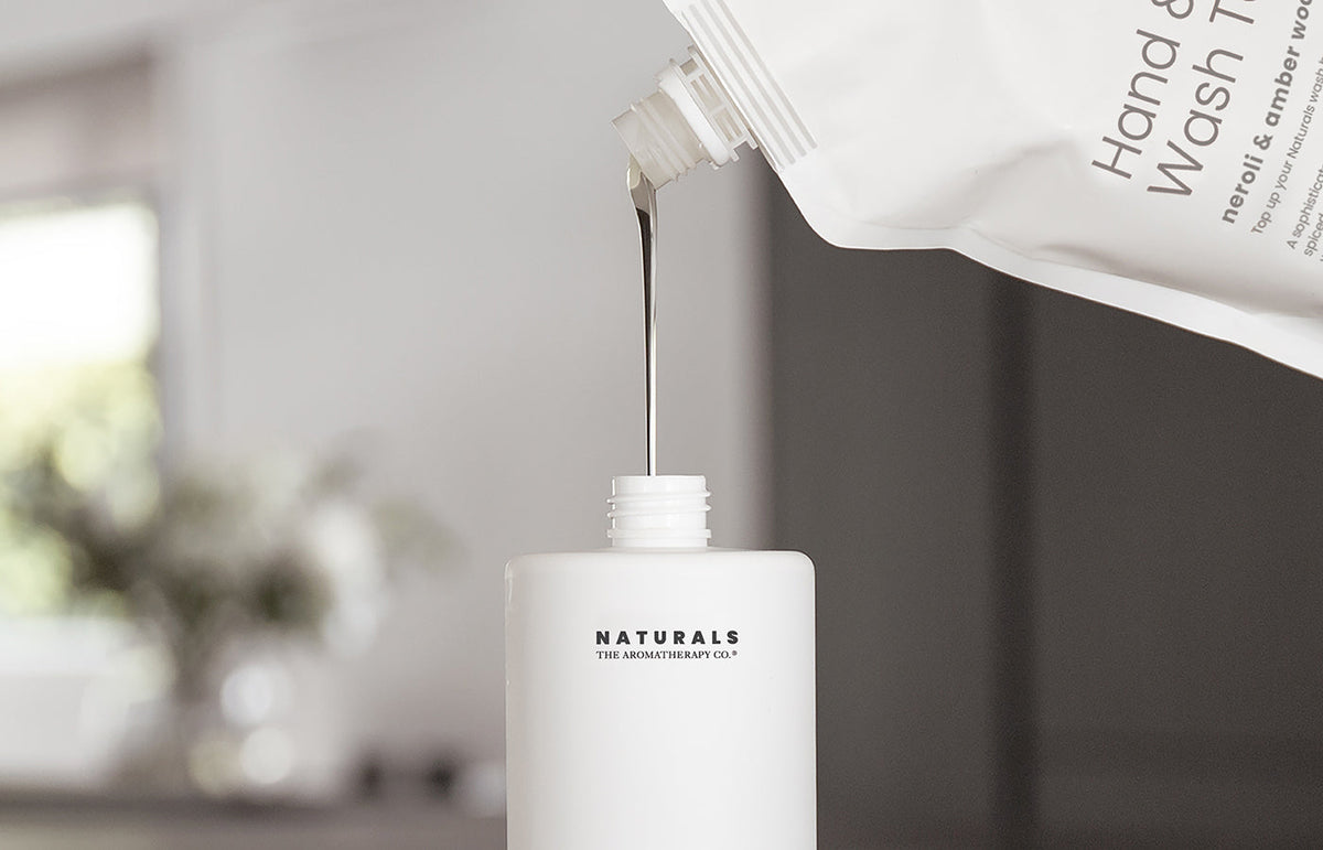 Wash being poured from a refill pouch into a white Naturals bottle, landscape crop