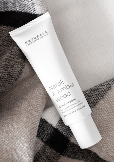Neroli & Amber Wood hand cream tube lying on a grey and black check wool throw