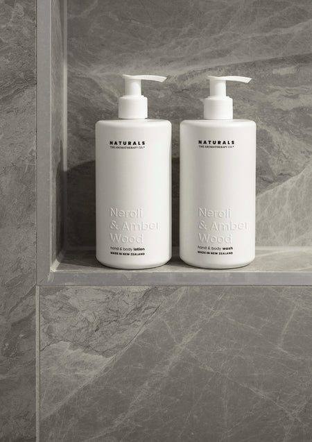Naturals Neroli & Amber Wood lotion and wash side by side in a grey marble shower niche