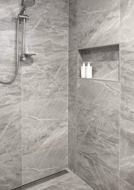 Grey marble walk-in shower with a chrome rail and two pump bottles in a recessed niche