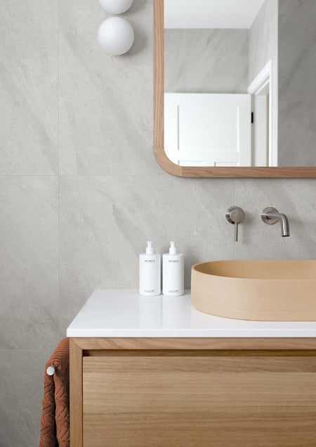 Bathroom with a round timber basin, oak vanity, arched mirror and two small pump bottles