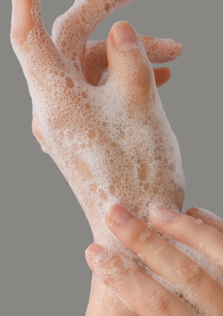 Hands lathering foamy wash against a grey background