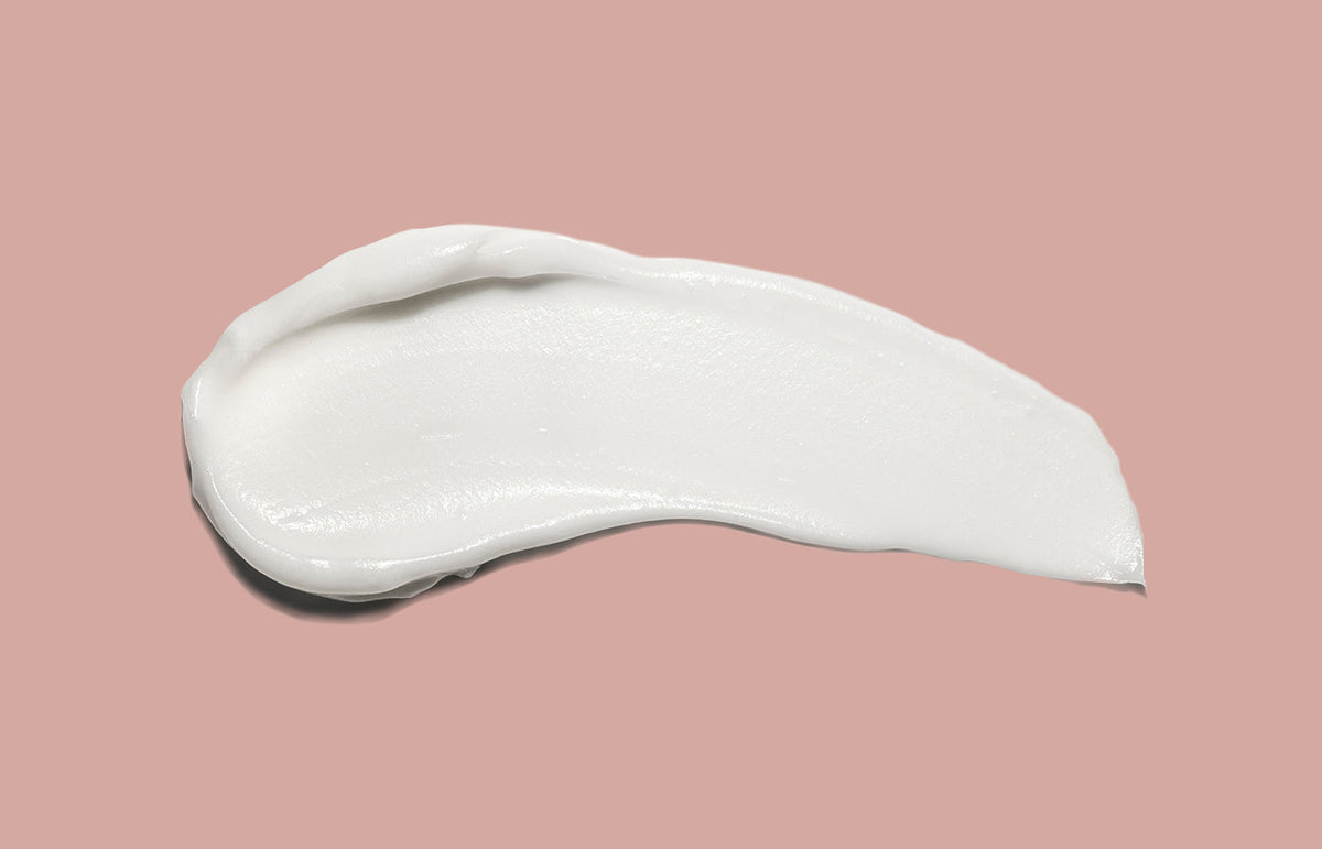 Swatch of white hand cream smeared across a dusty pink background