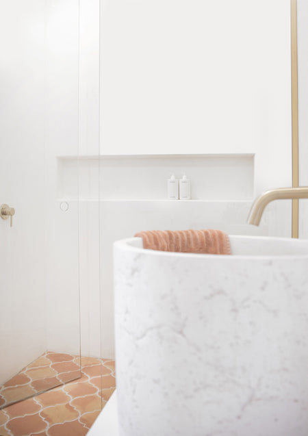 Bright bathroom with a white stone basin, brass tap, shower niche and terracotta floor tiles