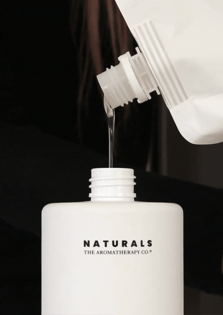 Naturals refill pouch being poured into a white pump bottle against a dark background