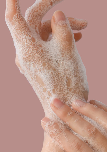Close view of lathered hands against a dusty pink background