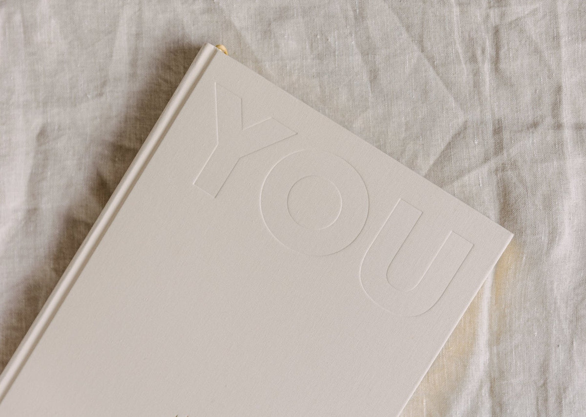 Close view of the cream YOU. journal on linen, showing the debossed YOU lettering on the cover
