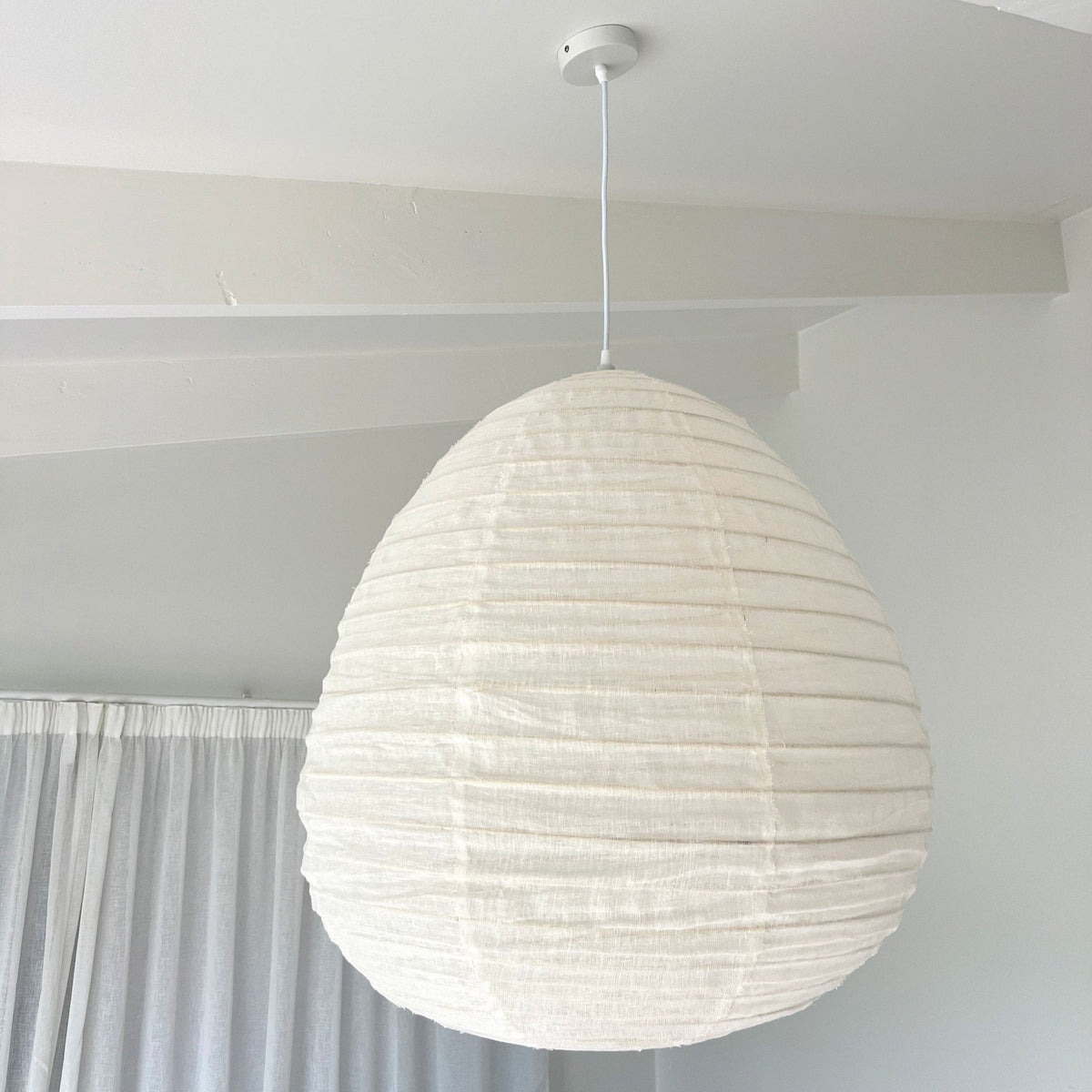 Pear linen pendant shade lit in a living room with sheer curtains