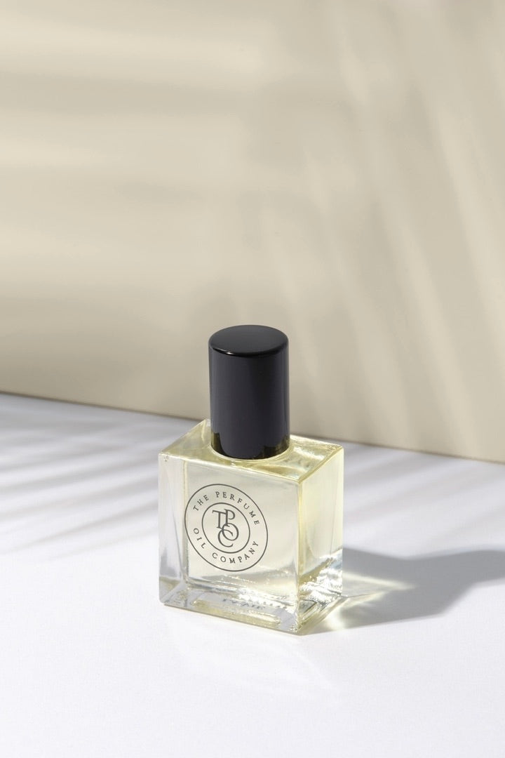 Pale amber perfume oil bottle with a black cap on a cream surface in soft shadow
