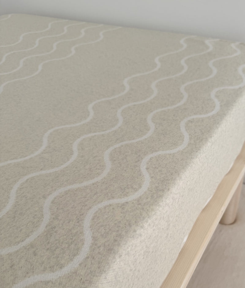 Coastal Marle jersey cotton fitted sheet stretched over a mattress, showing the ivory wave pattern