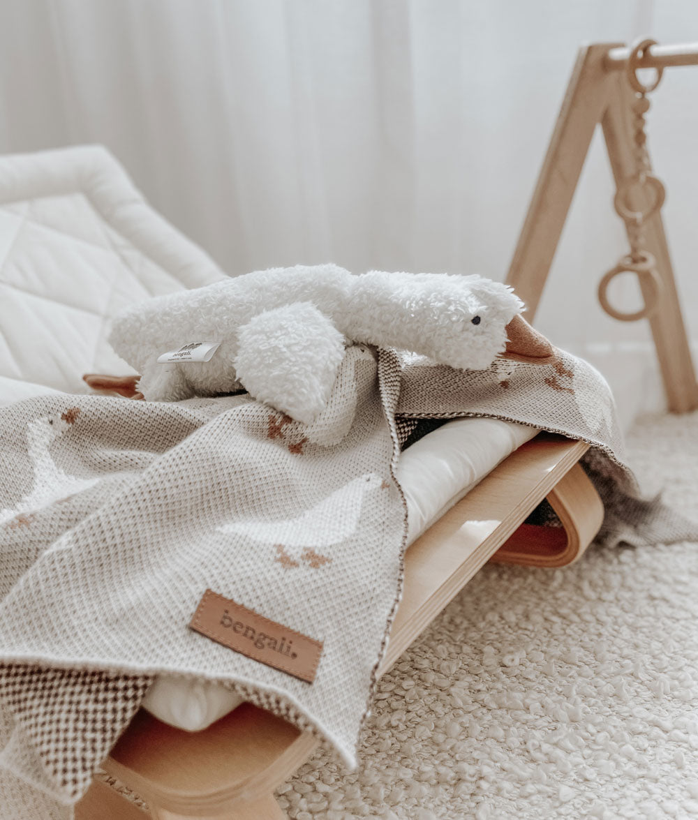 Ivory sherpa goose comforter draped over a knit blanket on a timber baby bouncer