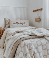 Bed with a salty days cushion, a sherpa throw and shell check bedding