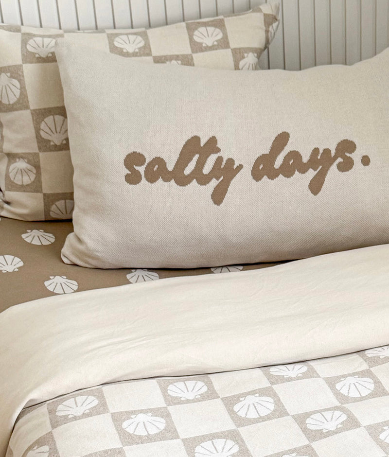 Close-up of the Salty Days cotton pillowcase in front of a shell check pillowcase on a shell print sheet