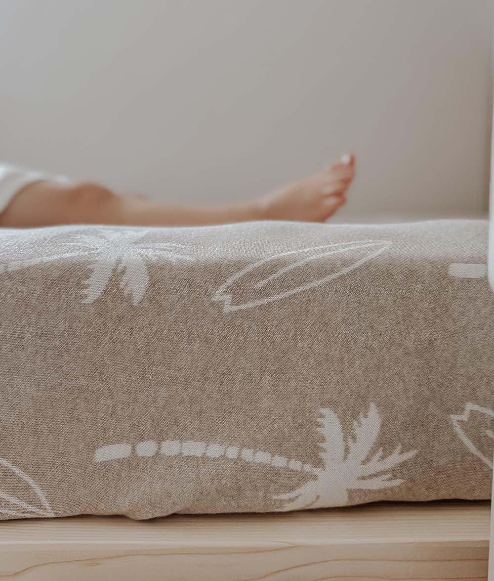 Dune jersey fitted sheet with ivory palms and surfboards stretched over a mattress