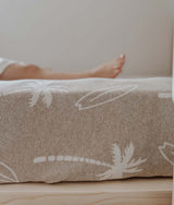 Dune jersey fitted sheet with ivory palms and surfboards stretched over a mattress