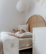 Child asleep on the dune palm fitted sheet in a room with a rattan headboard and white locker