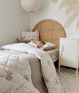 Child resting on a bed dressed in dune palm bedding with a quilted throw across it