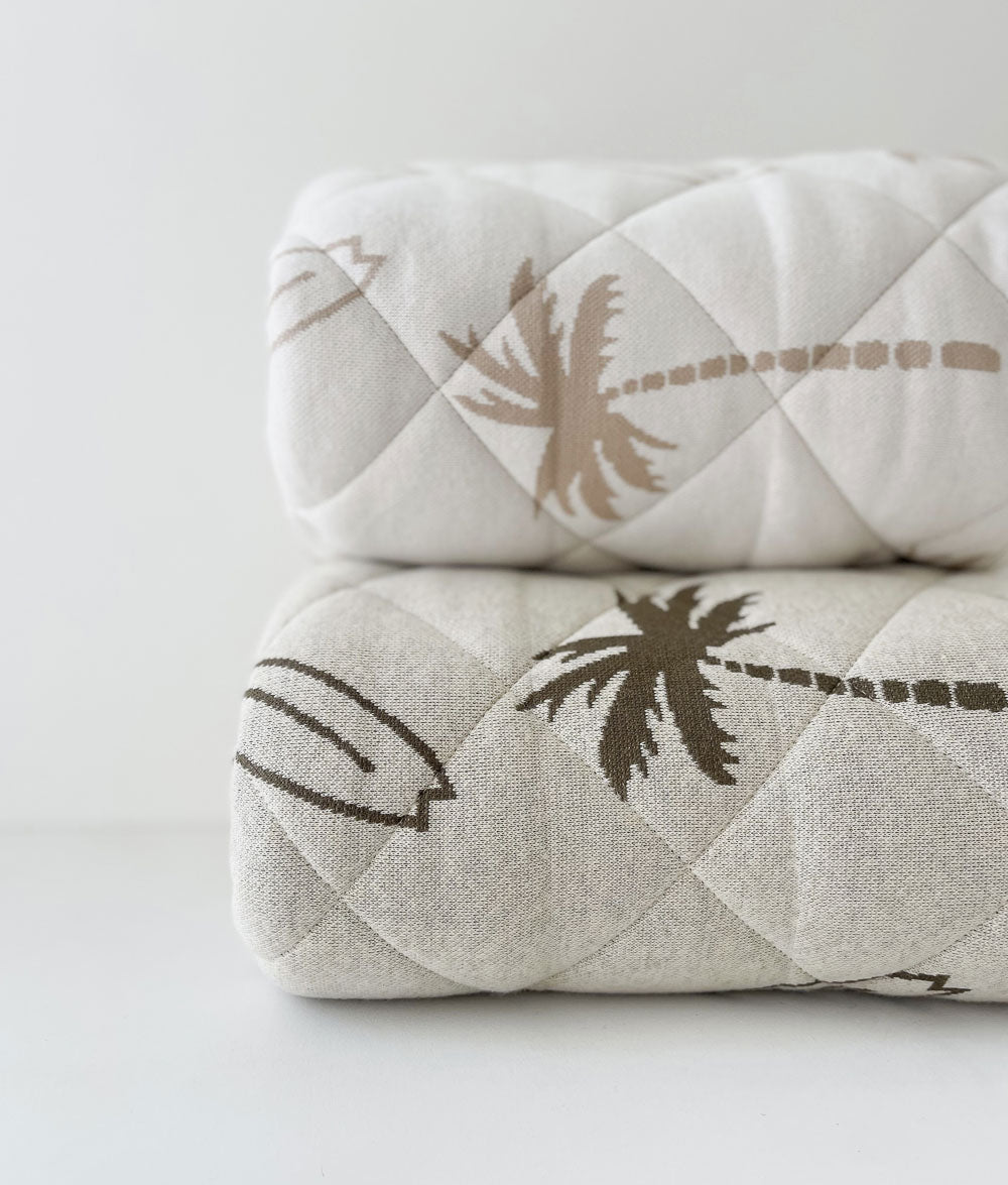 Two rolled Surfing Palm reversible kids quilts in the natural and olive prints on a white backdrop