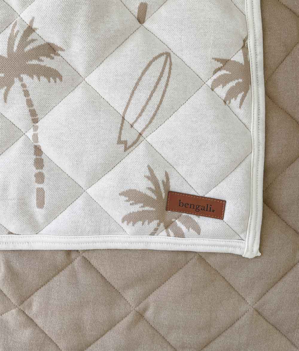 Corner of the natural Surfing Palm reversible quilt with leather label over its plain sand quilted reverse