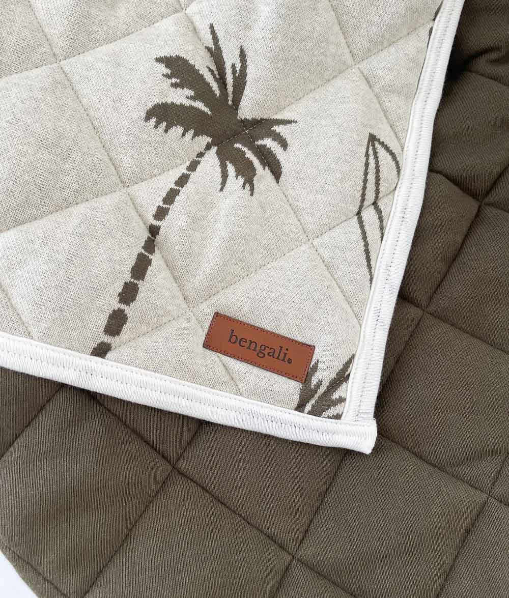 Close-up of the olive Surfing Palm reversible quilt with leather Bengali label and plain olive quilted reverse