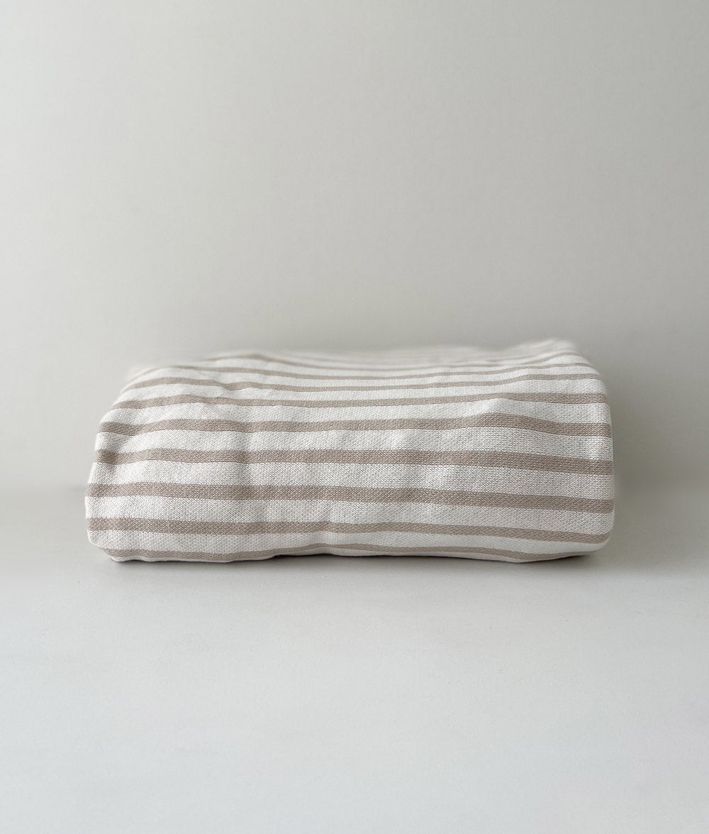 Folded greige pinstripe jersey cotton fitted sheet on a white backdrop