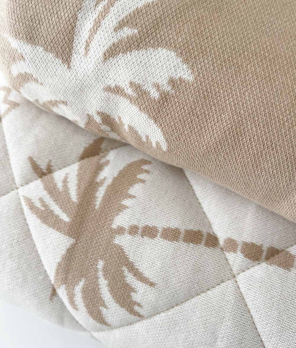 Close-up of the quilted Surfing Palm reversible quilt beneath a folded sand Surfing Palm fitted sheet