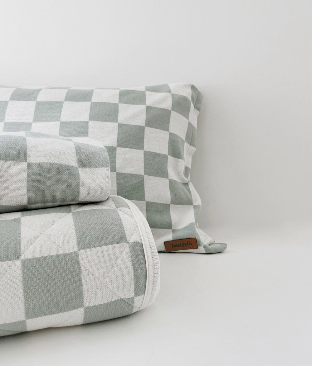 Sage Gingham pillowcase with a folded Sage Gingham fitted sheet and rolled quilt on white