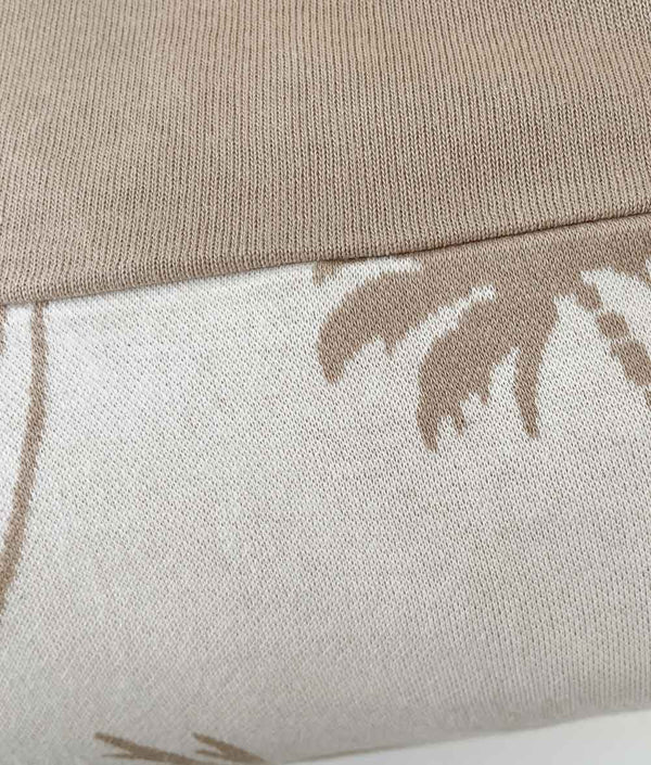 Close-up of a natural Surfing Palm kids pillowcase with sand palm print, a sand jersey sheet folded above