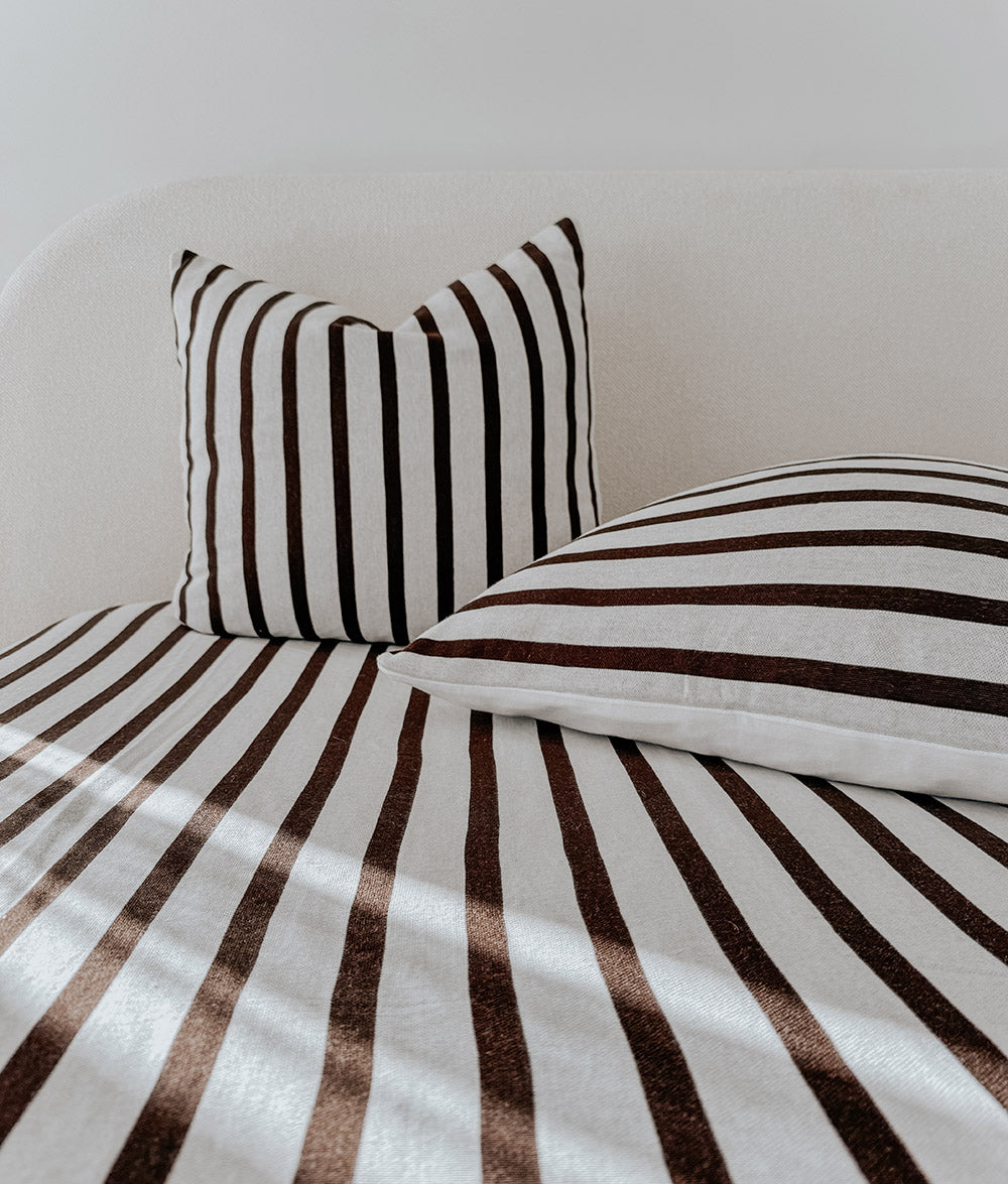 Chocolate and ivory striped euro pillowcase standing against a curved ivory headboard on a striped bed
