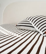 Striped euro pillowcase lying flat on a chocolate and ivory striped bed in soft daylight