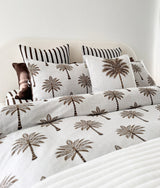 Striped euro pillowcases layered behind palm print cushions on a bed with palm print bedding