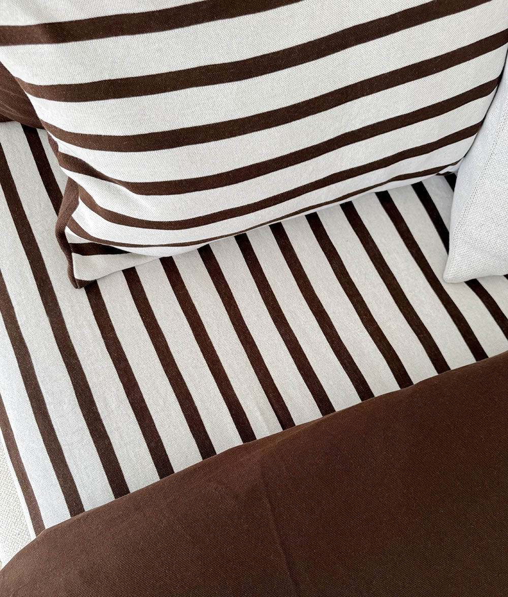 Sundown Stripe fitted sheet and striped pillows with a chocolate quilt folded across the end of the bed