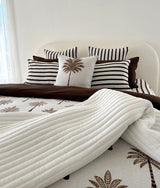Bed with striped pillowcases, a palm print cushion, chocolate quilt and ivory quilted throw
