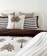Made bed with chocolate and ivory striped pillowcases behind a palm print cushion