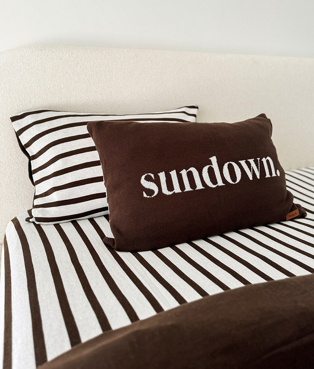 Chocolate sundown lumbar cushion sitting on the Sundown Stripe striped jersey fitted sheet